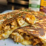 A close-up of two halves of Cozy Cheesy Garlic Chicken Wraps, showing melted cheese and seasoned chicken pieces inside a toasted tortilla.