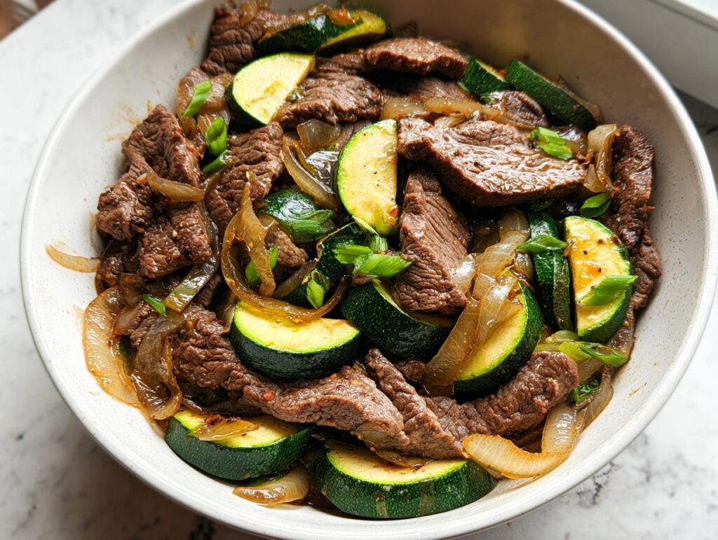 Close-up of a Cozy Grilled Steak Bowl with Zucchini, featuring sliced steak, sautéed onions, and bright green zucchini rounds.