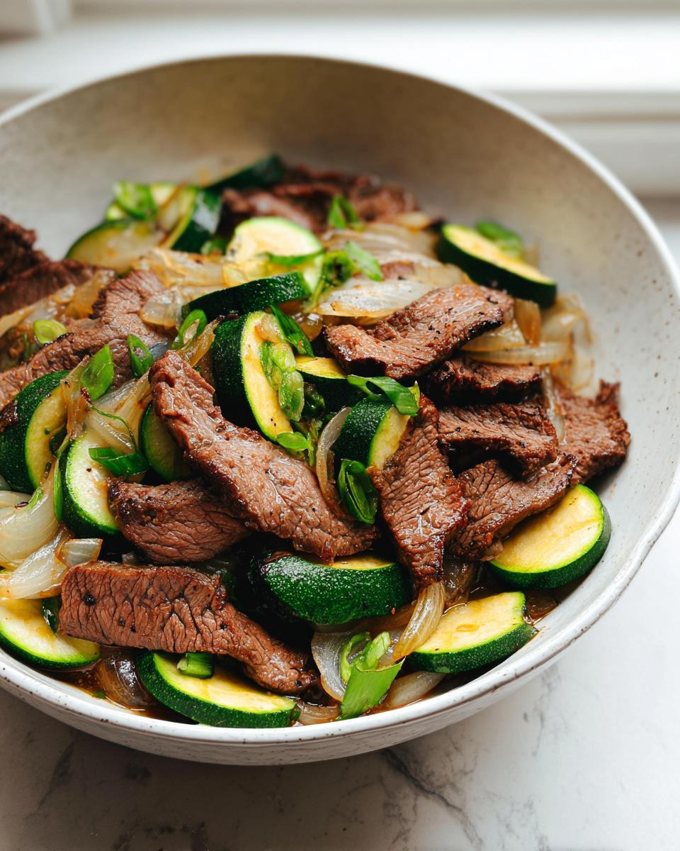 Close-up of a Cozy Grilled Steak Bowl with Zucchini, featuring sliced steak, sautéed onions, and bright green zucchini rounds.