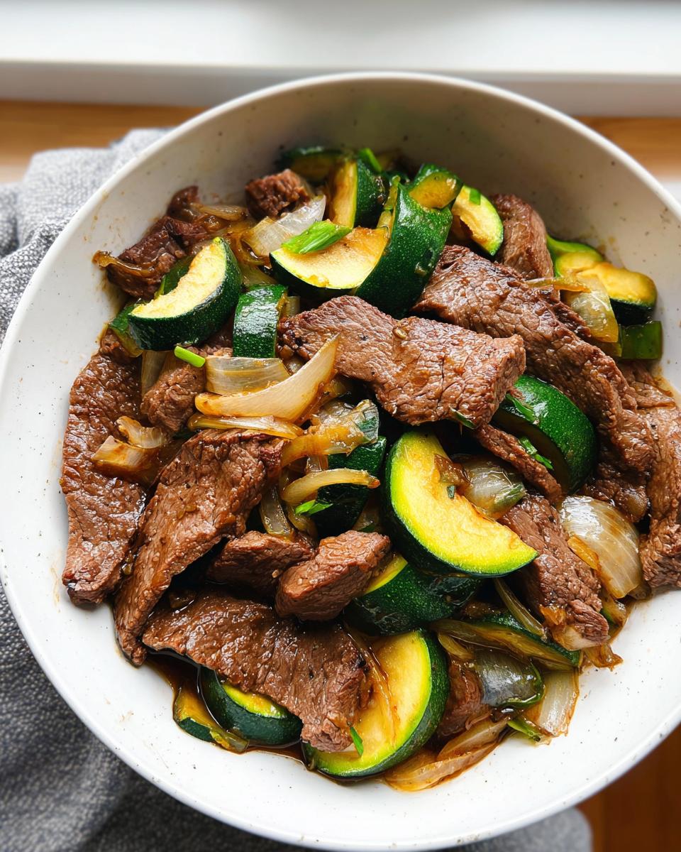 Close-up of a Cozy Grilled Steak Bowl with Zucchini, featuring sliced steak, green zucchini rounds, and sautéed onions in a white bowl.
