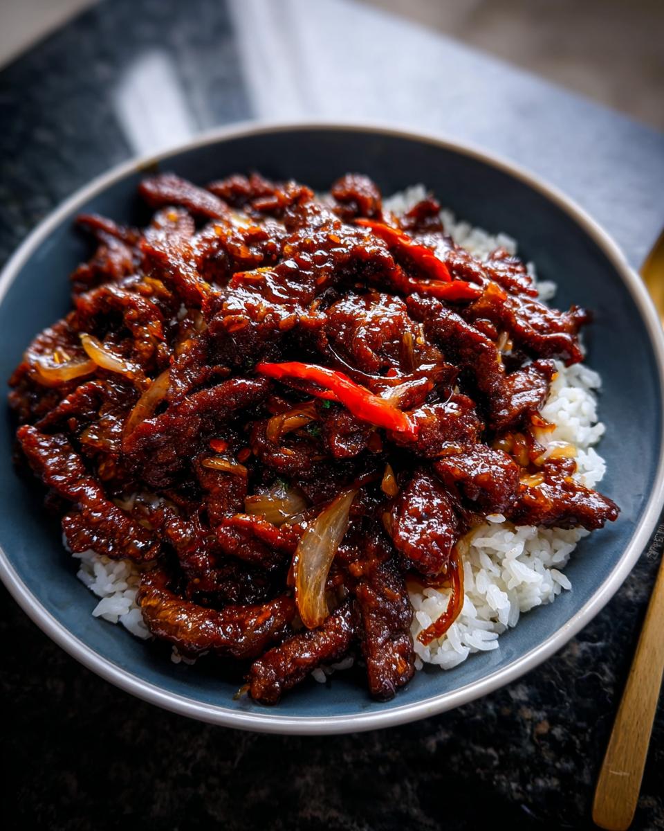 Close-up of a bowl filled with white rice topped generously with glossy Crispy Chilli Beef Rice.