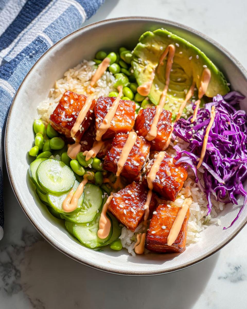 A close-up of a Crispy Salmon and Rice Bowl featuring glazed salmon cubes, avocado, edamame, and spicy mayo drizzle.