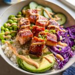 Close-up of a Crispy Salmon and Rice Bowl featuring glazed salmon cubes, white rice, avocado, edamame, and spicy mayo drizzle.