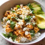 Close-up of an Easy Street Corn Chicken Bowl served over white rice, topped with cotija cheese and cilantro, with sliced avocado on the side.