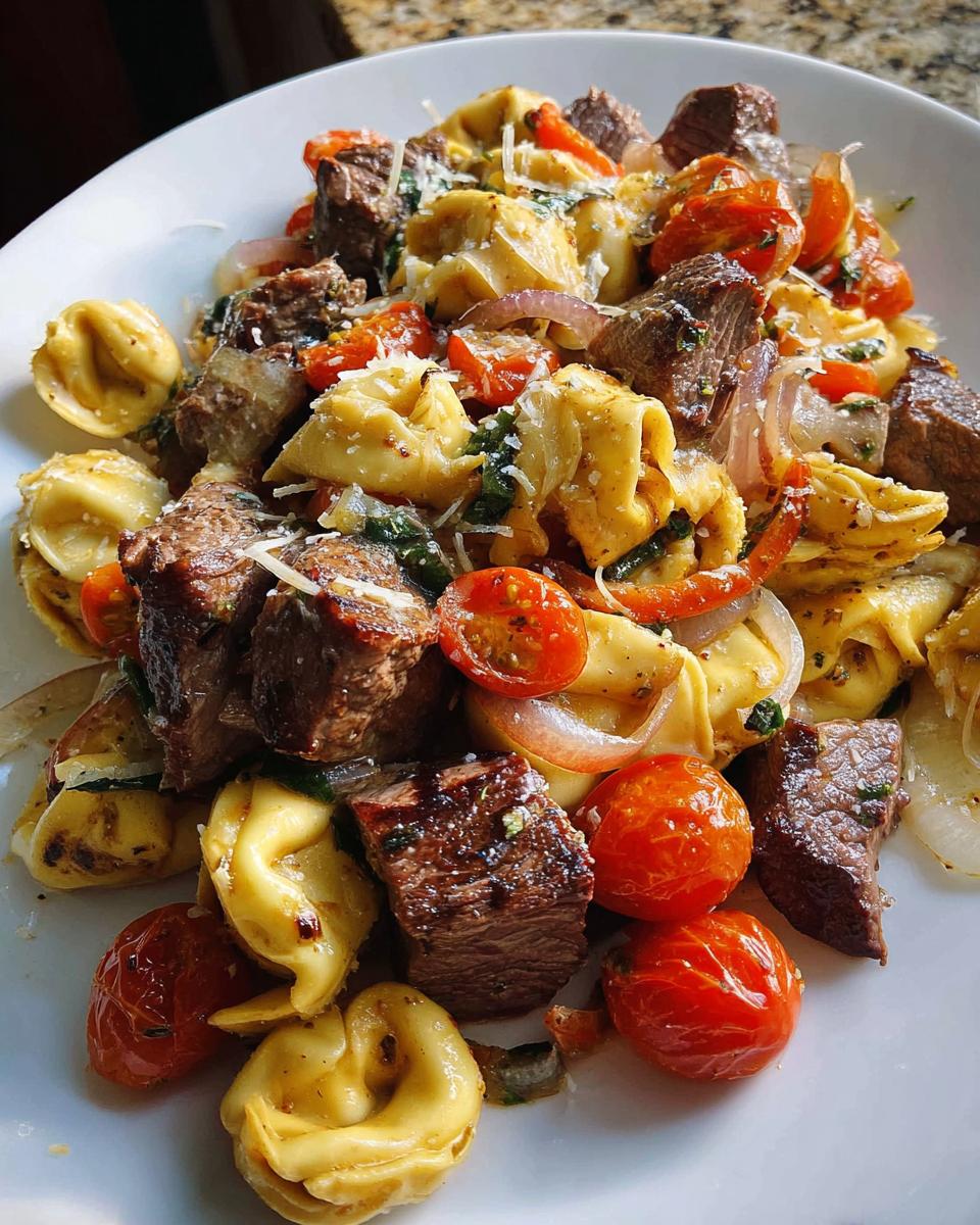 A close-up view of Garlic Steak Tortellini mixed with cherry tomatoes and red onions, topped with Parmesan cheese.