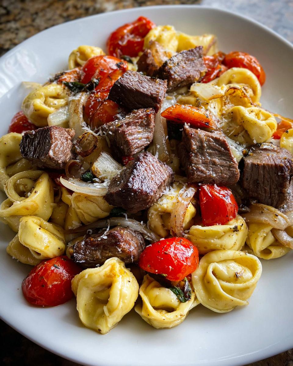 A close-up of Garlic Steak Tortellini mixed with roasted cherry tomatoes and onions, topped with grated cheese.