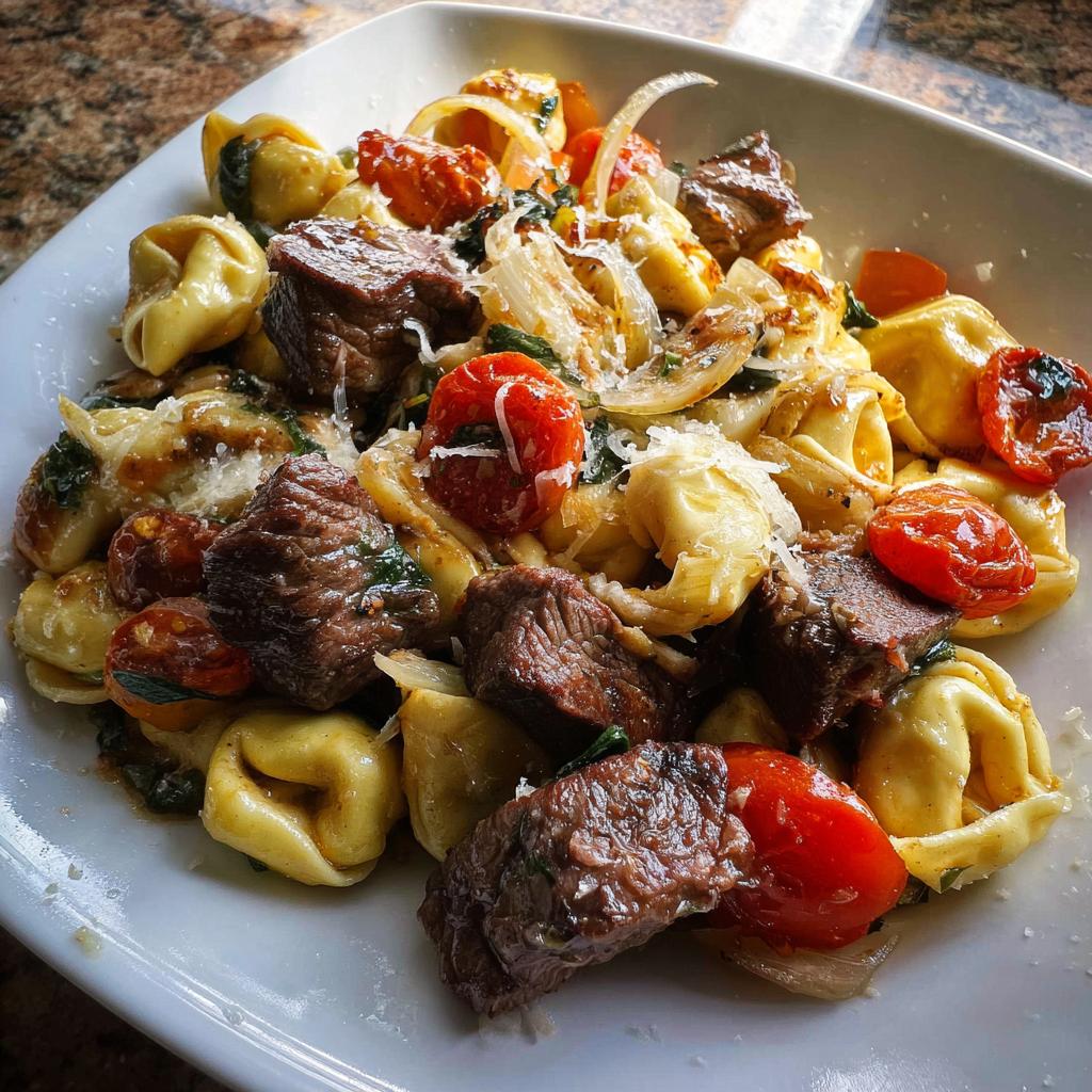 Close-up of Garlic Steak Tortellini mixed with roasted tomatoes, onions, and grated cheese.