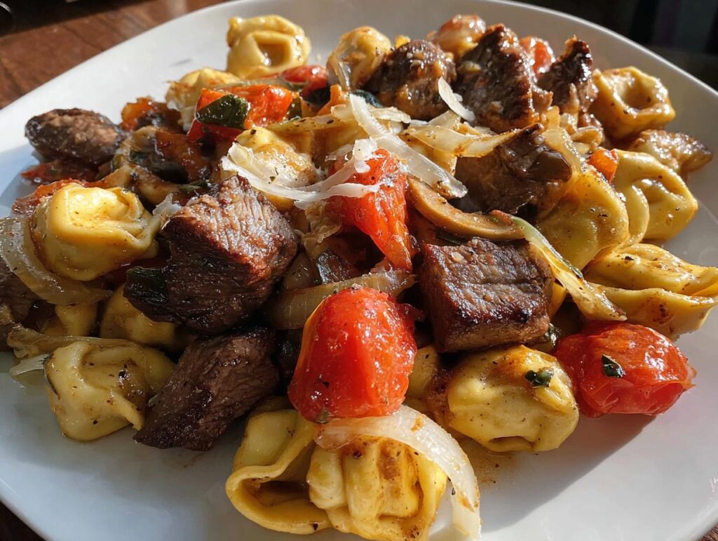 A close-up view of a serving of Garlic Steak Tortellini mixed with roasted tomatoes and onions, topped with shaved cheese.