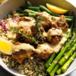 A close-up of a Healthy Lemon Garlic Chicken Meal Prep Bowl featuring seasoned chicken pieces, quinoa, asparagus, and a creamy sauce.