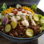 A close-up of a vibrant High-Protein Cheeseburger Bowls Recipe featuring ground beef, pickles, cheese, and sauce.