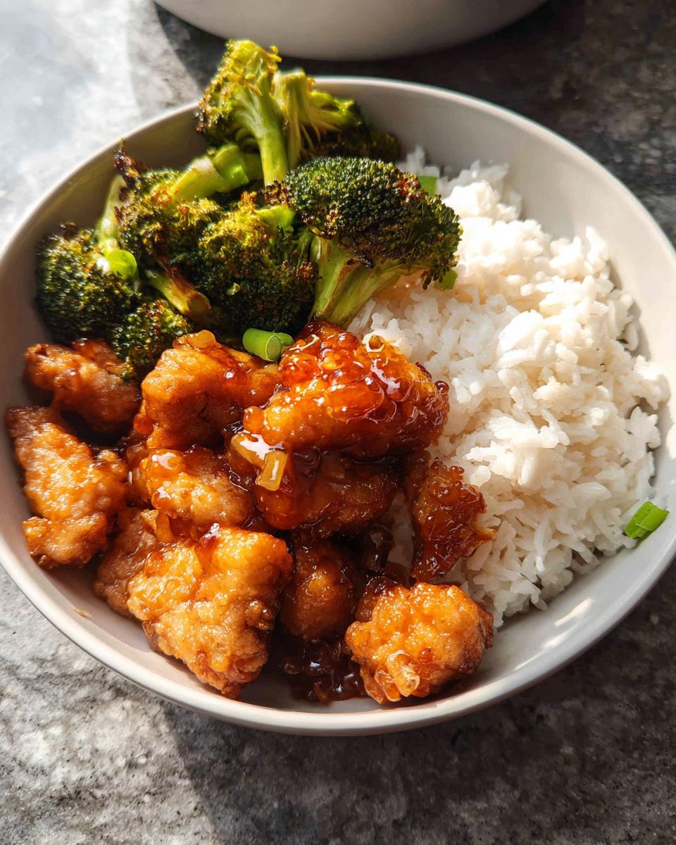 A bowl featuring crispy pork coated in honey garlic sauce, white rice, and roasted broccoli, making up a Honey Garlic Pork Rice Bowl.