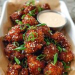 Close-up of Irresistible Sticky Honey Garlic Cauliflower Recipe pieces coated in glaze, topped with sesame seeds and green onions.