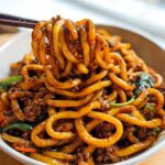 Chopsticks lifting thick, glossy noodles from a bowl of Irresistible Yaki Udon Noodle Recipe with ground meat and greens.