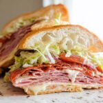 Cross-section of a loaded Italian Grinder Salad Sandwich showing layers of deli meats, melted cheese, shredded lettuce, and tomato.