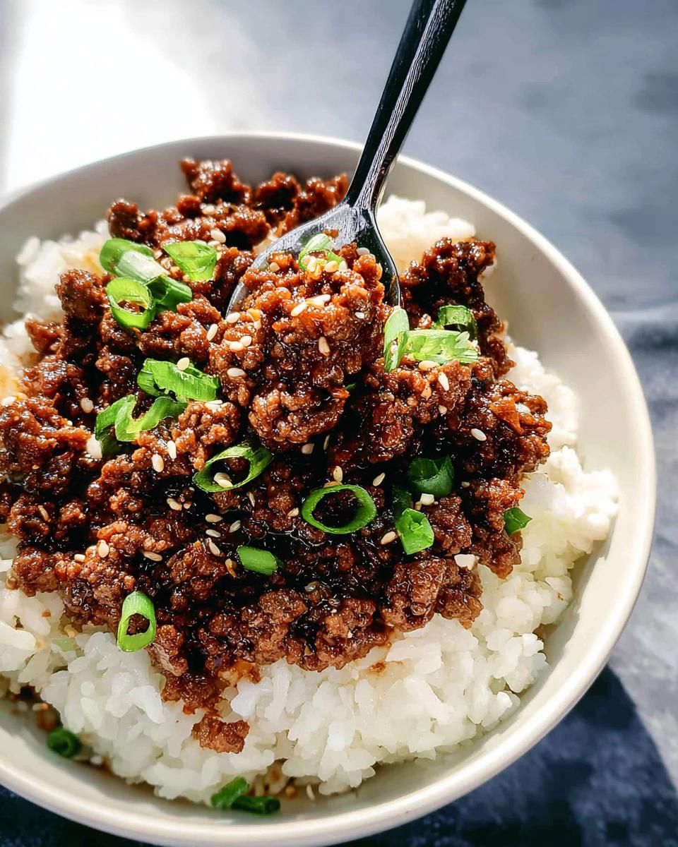 A spoonful of saucy Korean Ground Beef Bowl mixture served over white rice and garnished with green onions and sesame seeds.