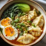 Overhead view of a hearty Savory Dumpling Ramen Bowl featuring ramen noodles, dumplings, soft-boiled eggs, and bok choy.