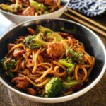 Close-up of a bowl filled with Spicy Garlic Chicken and Broccoli Noodle Bowls, featuring thick noodles, chicken pieces, and bright green broccoli florets.