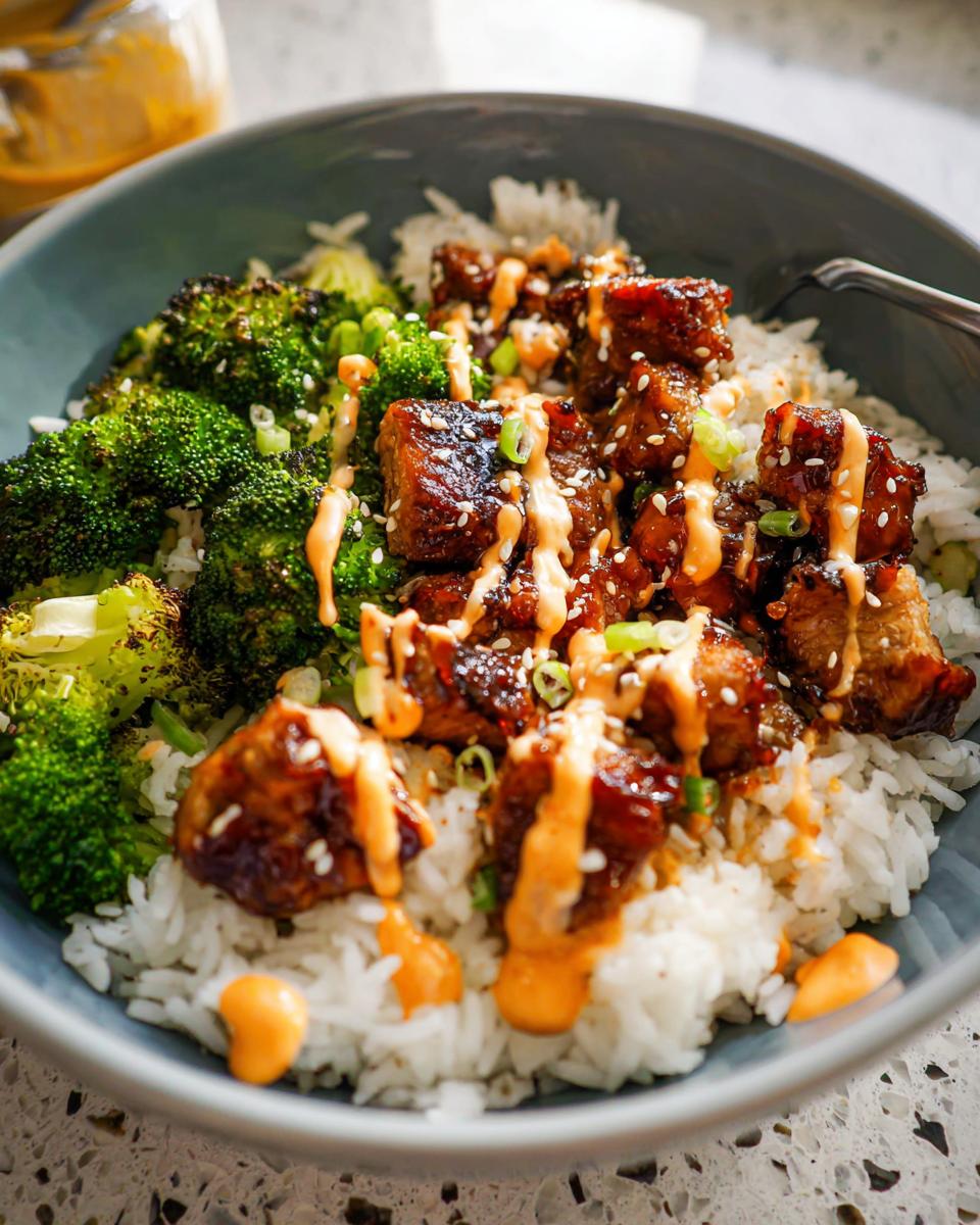 Close-up of Sticky Chicken Bowls featuring glazed chicken pieces over rice with roasted broccoli and a spicy orange drizzle.