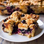 A close-up of two slices of the Best Blueberry French Toast Casserole on a white plate, with the rest of the casserole in the background.