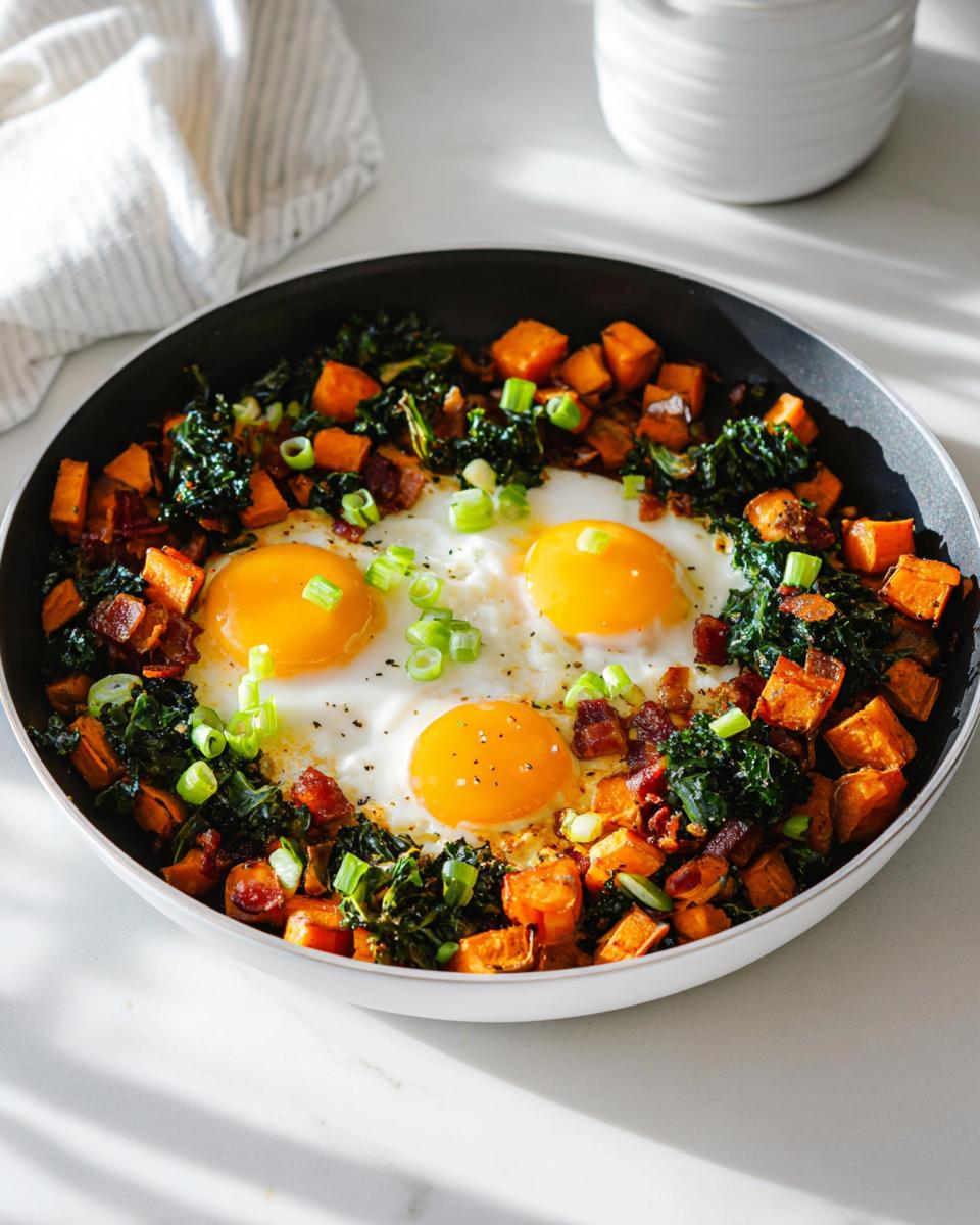 A one-pan BREAKFAST SWEET POTATO hash with fried eggs, kale, bacon, and green onions.