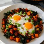A hearty one-pan BREAKFAST SWEET POTATO dish with two fried eggs, kale, bacon, and green onions.