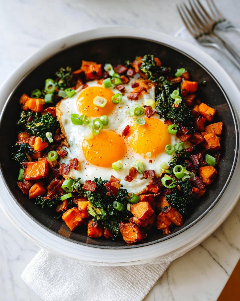 A close-up of a hearty one-pan BREAKFAST SWEET POTATO dish with fried eggs, kale, bacon, and green onions.