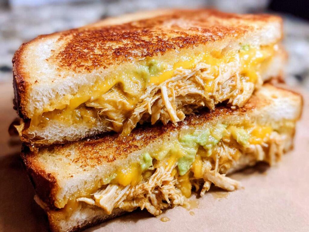 A close-up of a grilled Chicken Avocado Melt Sandwich, showing shredded chicken, melted cheese, and avocado.