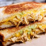 A close-up of a grilled Chicken Avocado Melt Sandwich, showing shredded chicken, melted cheese, and avocado.