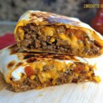 A close-up of a Chicken Crunch Wrap sliced in half, revealing seasoned ground meat, melted cheese, and a creamy filling.
