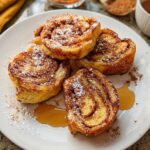 Close-up of Cinnamon Roll French Toast Bites dusted with powdered sugar and cinnamon, drizzled with syrup.