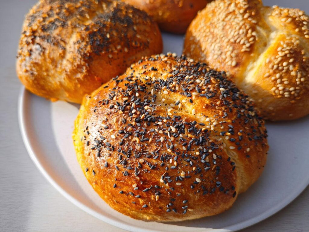 A close-up of four golden-brown cottage cheese flagels topped with various seeds, ready to be enjoyed.