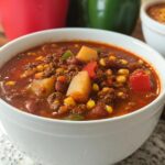 A close-up of a white bowl filled with hearty Cowboy Soup, featuring ground beef, potatoes, corn, and beans in a rich broth.