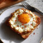 A single serving of crispy feta fried eggs on toast, seasoned with red pepper flakes and black pepper.