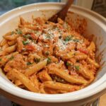 A close-up of Crock Pot Creamy Cajun Chicken Pasta in a white serving dish, garnished with shredded cheese and parsley.