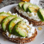 Two slices of EASY Avocado Toast with Cottage Cheese & Honey on a white plate, topped with fresh avocado slices and drizzled with honey.