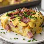 A slice of easy Eggs Benedict Casserole topped with creamy hollandaise sauce, crispy bacon, and chives.