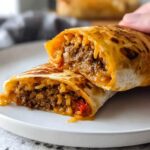 A close-up of an Easy Grilled Cheese Burrito Copycat Recipe cut in half, showing seasoned ground beef and rice filling with melted cheese.