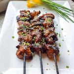 Three skewers of glistening Easy Japanese Chicken Yakitori, sprinkled with sesame seeds and chopped green onions.