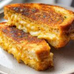 A close-up of a perfectly grilled Garlic Bread Grilled Cheese sandwich, oozing with melted cheese and sprinkled with herbs.
