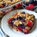 A slice of High Protein Triple Berry Bake on a white plate, topped with oats and mixed berries.