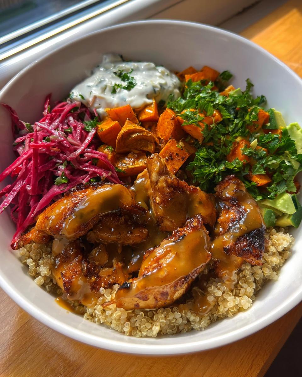 A vibrant Hot Honey Chicken Bowl featuring quinoa, roasted sweet potatoes, avocado, red cabbage slaw, and a dollop of yogurt sauce.