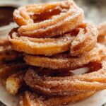 A close-up stack of Irresistible Spanish Churro Pancakes, coated in cinnamon sugar, with a bowl of chocolate sauce in the background.