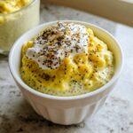 A close-up of a white bowl filled with vibrant yellow Lemon Cream Chia Pudding, topped with a dollop of cream and chia seeds.