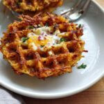 A golden-brown savory hashbrown chaffle with a fried egg and red onion in the center, garnished with parsley.