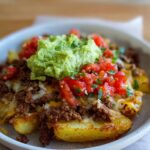 A close-up of a Schnelle Kartoffel Taco Bowl Meal Prep, featuring seasoned potatoes topped with seasoned ground meat, cheese, diced tomatoes, and guacamole.