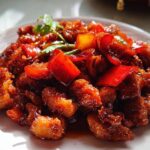 A plate of delicious Spicy Dragon Chicken, glistening with sauce and mixed with red bell peppers and green chilies.