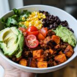 A vibrant Sweet Potato Taco Bowl filled with seasoned ground meat, roasted sweet potato cubes, black beans, corn, avocado slices, and cherry tomatoes.