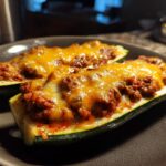 Two baked zucchini boats filled with seasoned ground beef and topped with melted cheese.