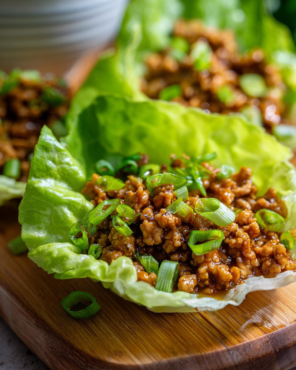 Close-up of fresh chicken lettuce wraps filled with seasoned ground chicken and topped with chopped green onions.