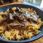 A close-up of a creamy beef stroganoff skillet meal served over fusilli pasta, featuring tender beef chunks and mushrooms in a rich sauce.